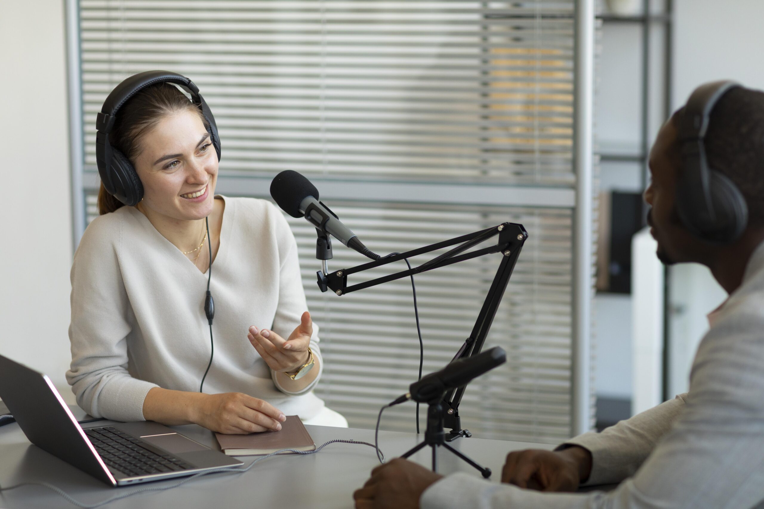 Two professionals, one man and one woman, talking on a podcast with a laptop and notepad.