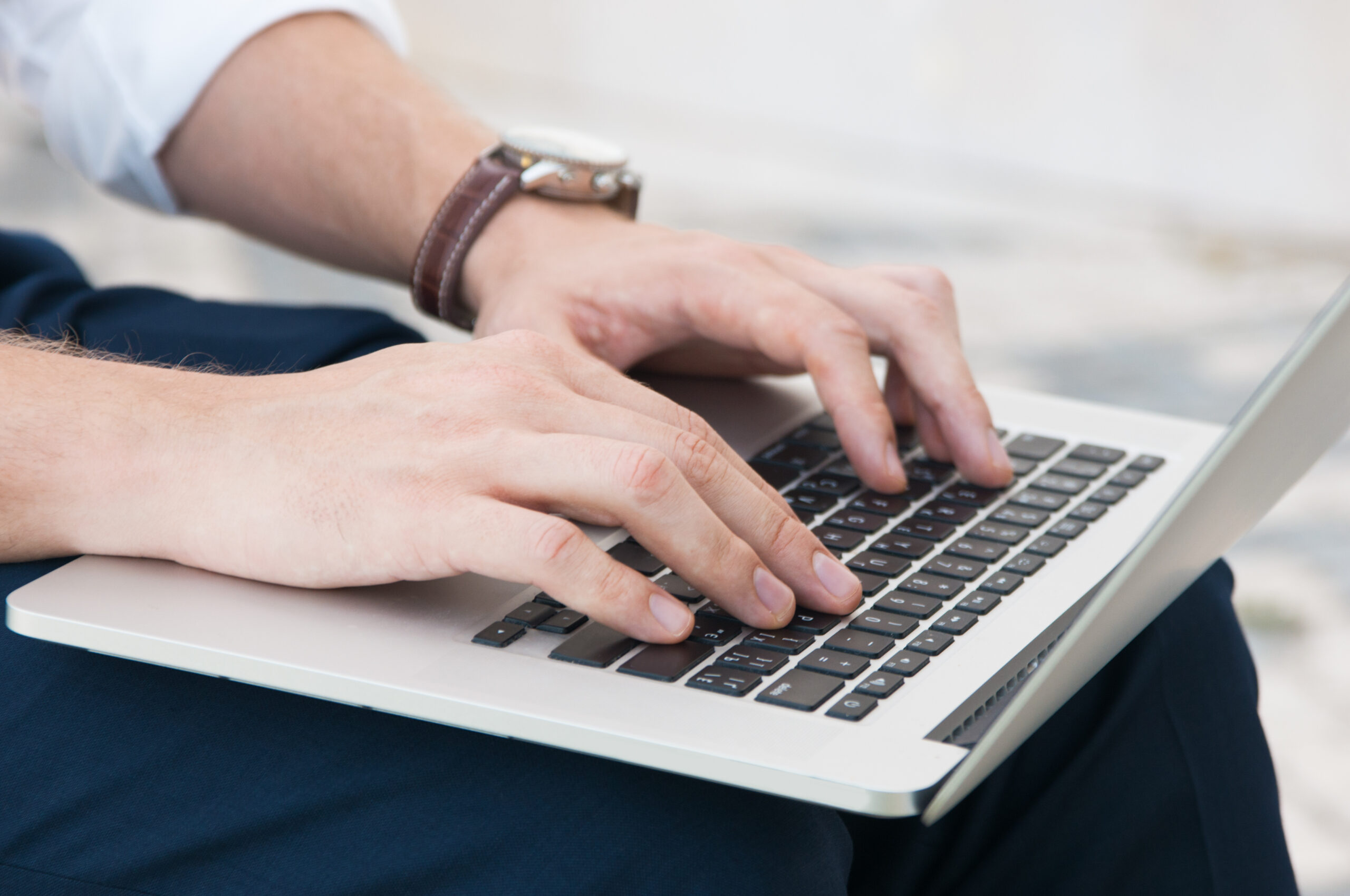 Closeup of business man working on laptop outdoors. Guy sitting with laptop computer on his lap and blurred view in background.